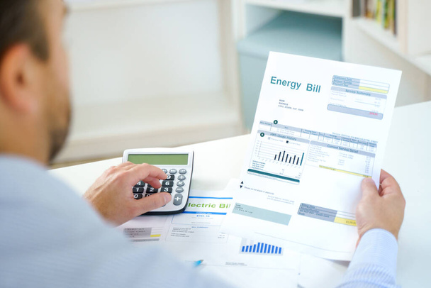 Человек, рассчитывающий расходы на электроэнергию дома и документ выписки счета - Фото, изображение