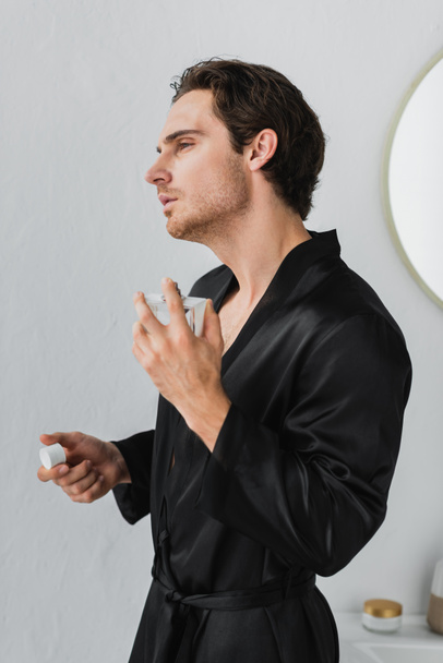 Young man in satin robe applying perfume in bathrobe  - Zdjęcie, obraz