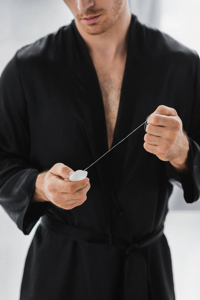 Cropped view of man in black robe holding dental floss at home  - Foto, Imagem