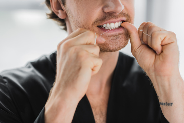 Άποψη ενός άνδρα με μαύρη ρόμπα που καθαρίζει τα δόντια με οδοντικό νήμα  - Φωτογραφία, εικόνα