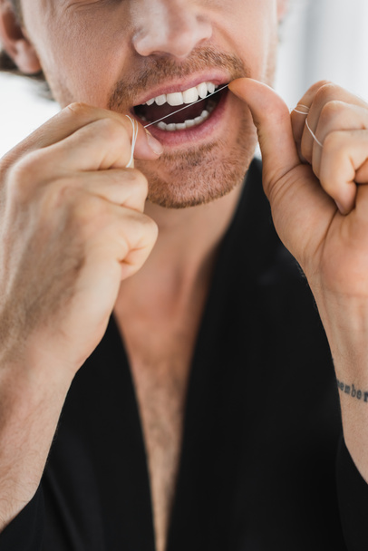 Обрезанный вид человека в черном халате, чистящего зубы зубной нитью  - Фото, изображение