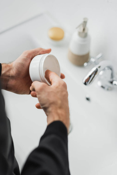 Cropped view of man taking cosmetic cream from jar in bathroom  - Фото, зображення