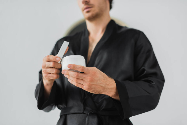 Cropped view of blurred man in robe holding cosmetic cream in bathroom  - Foto, Imagen