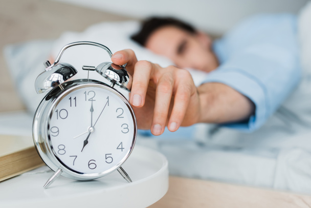 Blurred man switching alarm clock on bedside table in morning  - Φωτογραφία, εικόνα