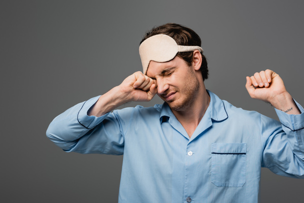Young man in pajama and sleep mask stretching isolated on grey  - Photo, Image