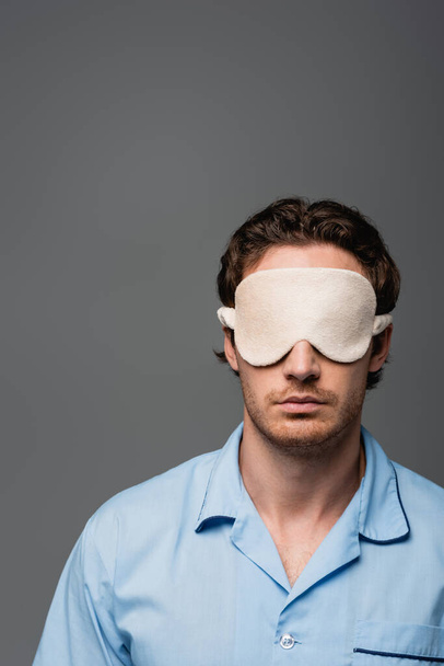 Young man in pajama and sleep mask standing isolated on grey  - Foto, imagen