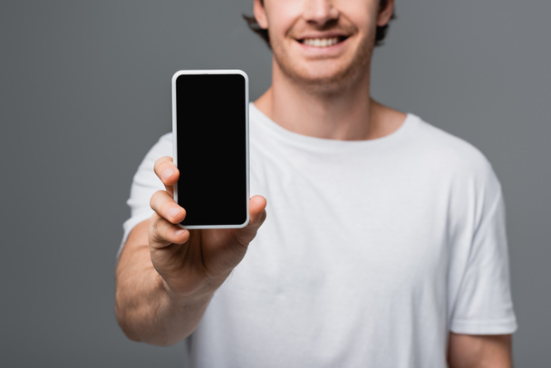 Cropped view of smartphone in hand of blurred smiling man isolated on grey  - 写真・画像