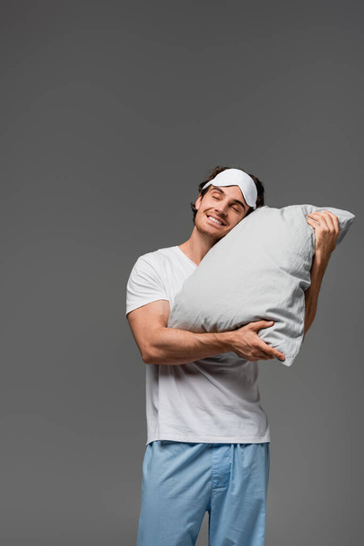 Happy man in pajama holding pillow isolated on grey  - Фото, изображение