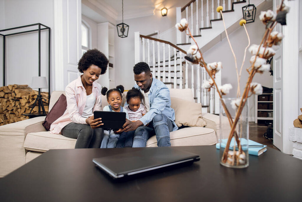 African parents with kids using tablet while resting on couch - Valokuva, kuva