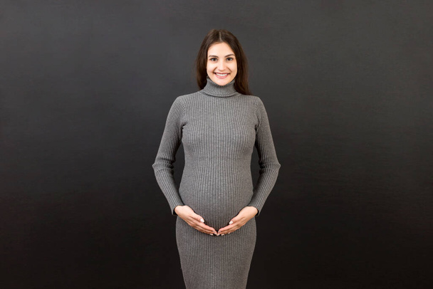 Mujer embarazada feliz tocando su abdomen en fondo de color. Futura madre. Esperando un bebé. Copiar espacio. - Foto, imagen