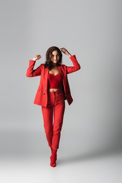 full length of young pleased woman in red boots and suit posing on grey - Foto, imagen