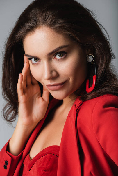young trendy woman in red suit and earring posing isolated on grey - Fotó, kép