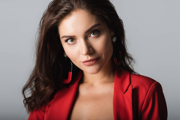 young woman in red suit and earrings looking at camera isolated on grey - Foto, immagini