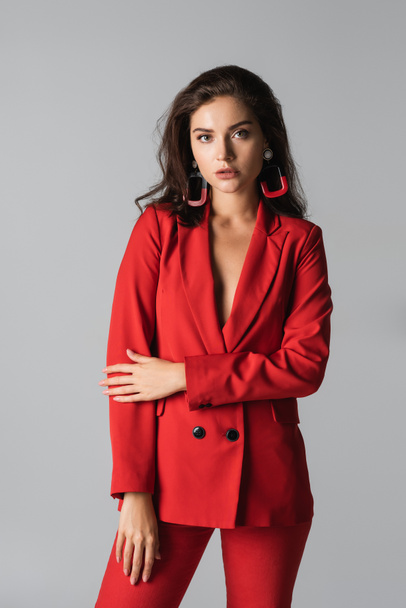 stylish woman in red outfit posing and looking at camera isolated on grey  - Fotografie, Obrázek
