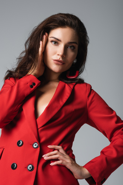 low angle view of stylish woman in red suit posing with hand on hip and looking at camera isolated on grey  - Foto, immagini