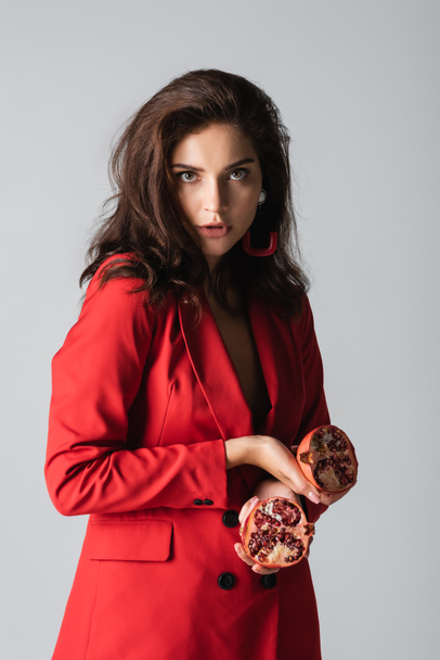 brunette woman in trendy suit holding red pomegranate isolated on grey - Valokuva, kuva