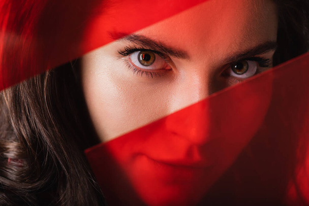 close up of young woman looking at camera through red glass  - Fotografie, Obrázek