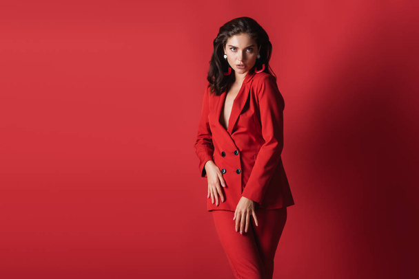 young brunette model in suit posing while looking at camera on red - Foto, Imagem