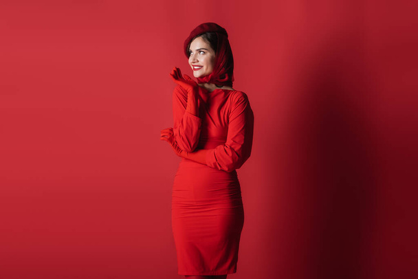 happy and elegant woman in beret and dress posing on red - Foto, imagen