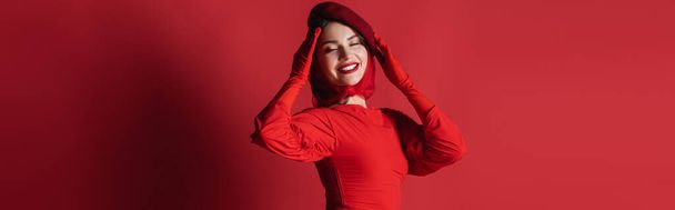 joyful and elegant woman in beret and dress posing on red, banner - Photo, image