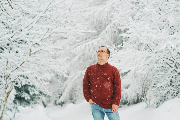 Outdoor portrait of middle age 55 - 60 year old man enjoying nice cold weather in winter forest, wearing red knitted pullover - Photo, Image