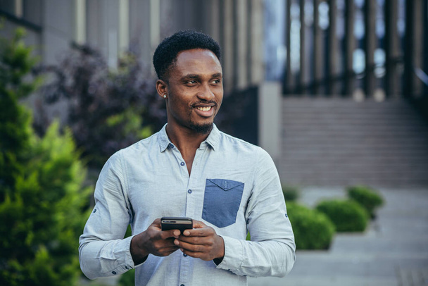 Young happy african american male freelancer corresponding in mobile and reading good news from mobile phone online - Фото, зображення