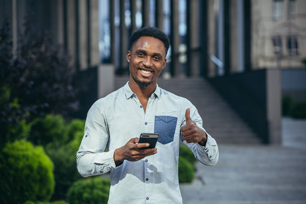Charming african american man happy looking at camera, holding mobile phone in hands smiling and happy - Фото, изображение