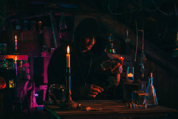 stregone alchimista in abiti scuri è impegnato nella produzione di pozioni in un laboratorio artigianale - Foto, immagini