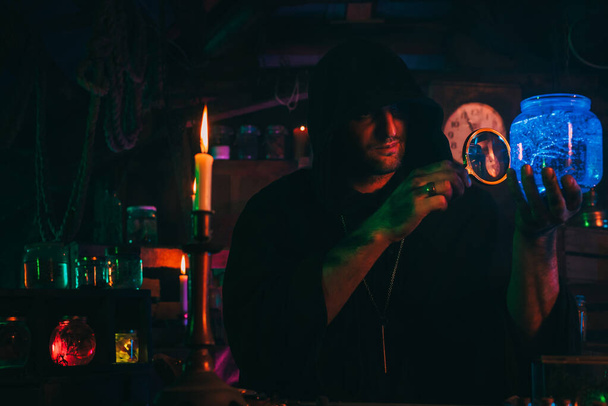 varázsló alkimista sötét ruhában részt vesz bájital készítés egy kézműves műhelyben - Fotó, kép