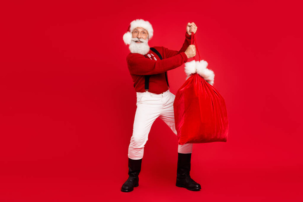 Full length photo of santa claus happy positive smile hold bag present newyear isolated over red color background - Φωτογραφία, εικόνα
