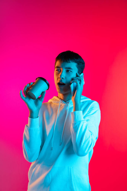 Studio shot of young boy, student, teen in casual clothes using phone isolated on magenta backgroud in neon light. - Photo, image