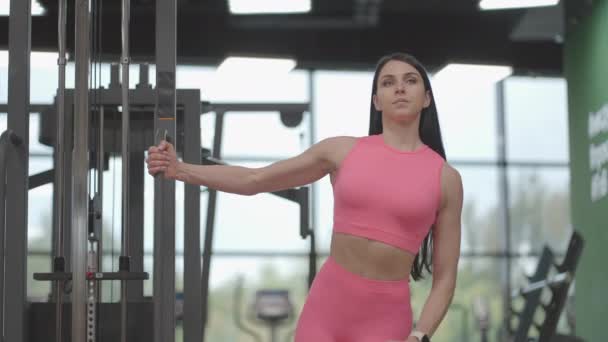 A young woman in a crossover raises her shoulder arms in a pink suit. Exercises for training the arms and shoulders - Footage, Video