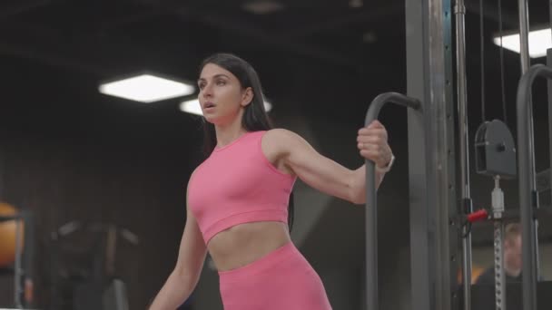 Eine junge Frau im Crossover hebt im rosafarbenen Anzug die Schultern. Übungen zum Training der Arme und Schultern - Filmmaterial, Video