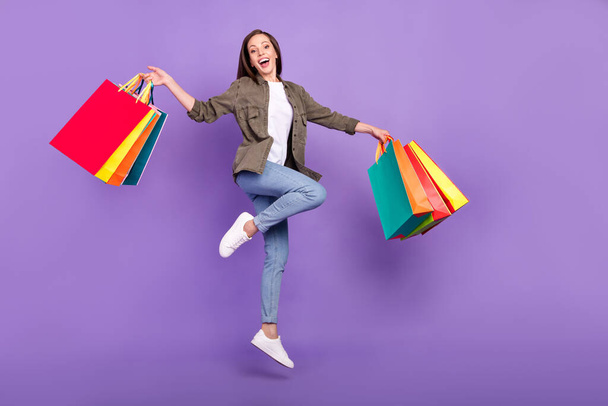 Full length body size photo woman jumping up happy keeping bags in shopping center isolated pastel purple color background - Foto, Imagen