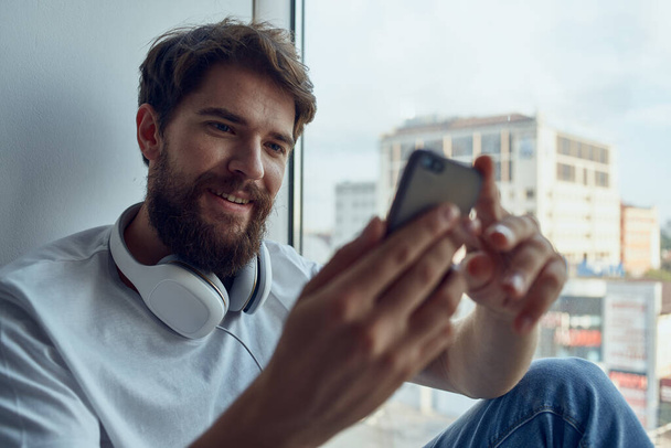 man in white t-shirt sitting near the window in headphones listening to music - Foto, immagini