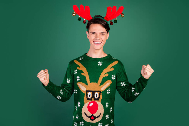 Photo of cheerful astonished guy celebrate victory wear horns deer ornament pullover isolated green color background - Zdjęcie, obraz