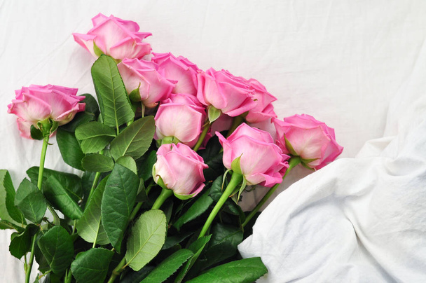 Букет розовых роз на белом белье на кровати  - Фото, изображение