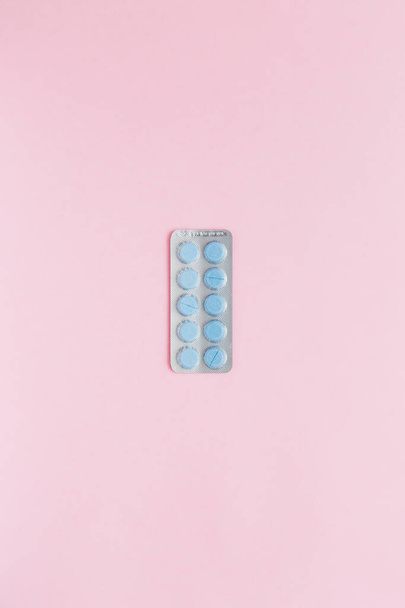 Волдырь с голубыми таблетками на розовом фоне, вид сверху. Концепция медицины, биография. Вертикальное фото. Копирование пространства. - Фото, изображение