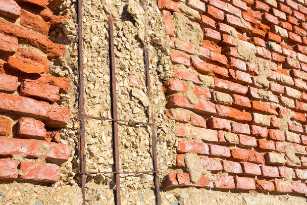 Ancienne structure en béton armé et dangereux avec des barres d'armature métalliques endommagées et rouillées contre un mur de briques endommagé et endommagé. - Photo, image