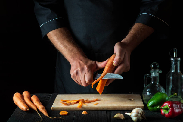 Šéf loupe mrkev na zeleninovou polévku v kuchyni restaurace. Detailní záběr - ruce kuchaře při práci. Mrkvová strava - Fotografie, Obrázek