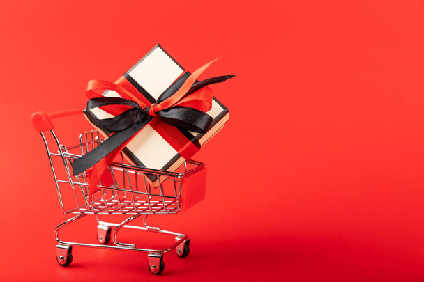 red shopping cart with a gift box on a red background, with copy space. - Foto, Imagem