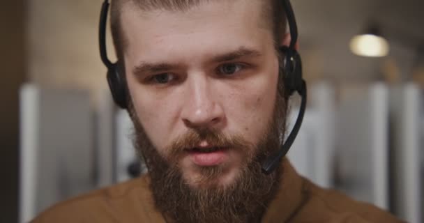 Call center worker - a young man in headphones communicates with a client - Кадры, видео
