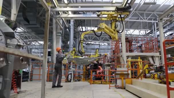 BELARUS, BORISOV - 29 de septiembre de 2021: Ensamblaje moderno de automóviles en la planta, los trabajadores de fábrica en uniforme colocan la capucha en el automóvil en la planta - Metraje, vídeo