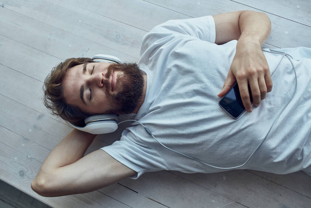 man in white t-shirt lying on the windowsill wearing headphones hipster - Photo, Image