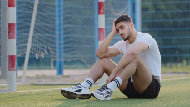 目標に対してサッカー場の芝生の上に座っている中東のサッカー選手を吹いて不満を抱くゲームを熟考し、夏のスポーツウェアの不満スコアで千年運動選手、失望した結果 - 映像、動画