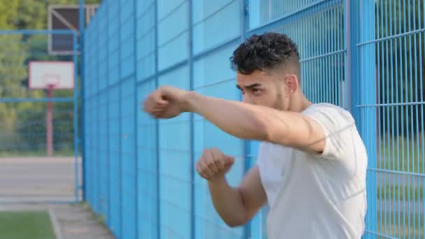 Serio enfocado joven árabe hispano atleta boxeador agitando las manos con los puños apretados que muestran la técnica de perforación. Oriente Medio chico indio entrenamiento en el estadio, fanático del fútbol se preparan para luchar - Imágenes, Vídeo