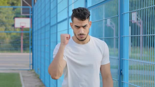 Разгневанный фанат футбола молодой арабский латиноамериканец машет рукой сжатым кулаком, ближневосточный индиец угрожает соперникам, демонстрирует агрессивное поведение, силу и агрессию - Кадры, видео