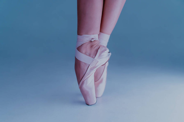 Ballet dancers feet, how she practices in pointe shoes exercises on blue background. Beautiful womans legs. Ballerina shows classic ballet pas. - Fotó, kép
