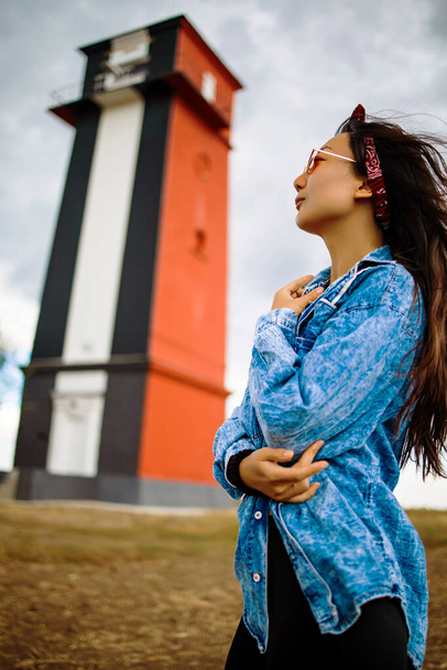 Mujer asiática turismo faro paisaje marino en Europa viajes recreación al aire libre concepto de estilo de vida. chica pelo en el viento usando una chaqueta de mezclilla - Foto, imagen