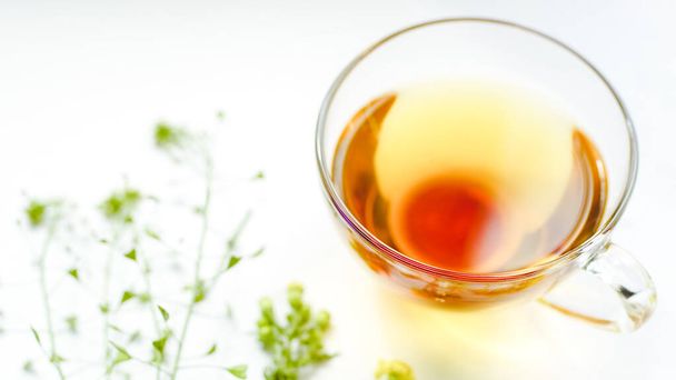 Herbata ziołowa w szklanej filiżance. Zioła i kwiaty na białym stole - Zdjęcie, obraz